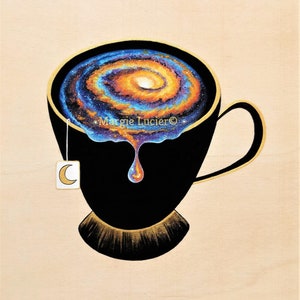 Op de afbeelding: Een zwarte theekop met een gouden rand en handvat, gevuld met een draaiende, galaxie-achtige patroon in tinten blauw, oranje en geel. Een enkele druppel van de galaxie-achtige vloeistof druppelt uit de kop. Een wit theezakje met een halve maan ontwerp hangt aan de zijkant van de kop. De tekst "Margie Lucier&copy;" is zichtbaar op de kop.