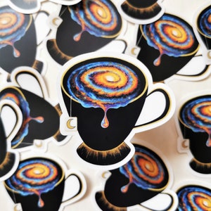 Pu&ograve; includere: Un set di adesivi con una tazza da t&egrave; nera piena di una galassia vorticosa, con un bordo dorato e una bustina di t&egrave; che cola. La galassia &egrave; un mix di colori blu, arancioni e gialli.