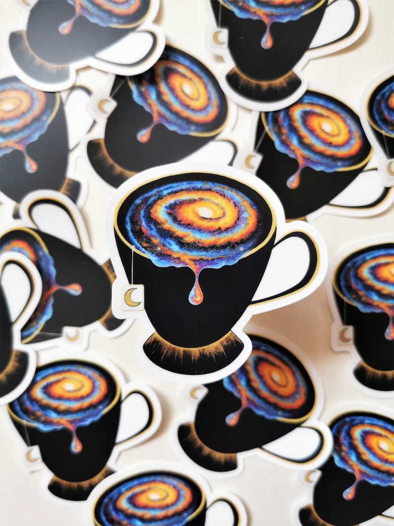 Pu&ograve; includere: Un set di adesivi con una tazza da t&egrave; nera piena di una galassia vorticosa, con un bordo dorato e una bustina di t&egrave; che cola. La galassia &egrave; un mix di colori blu, arancioni e gialli.