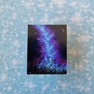 May include: A painting of a dark blue and purple galaxy with a shooting star in the upper right corner. The galaxy is over a silhouette of tall grass.