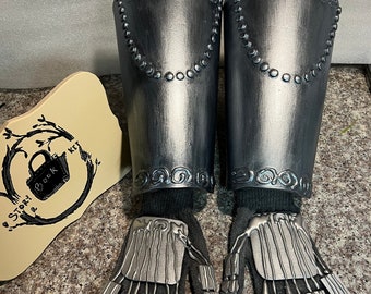 May include: A pair of silver-colored metal forearm guards with black fabric lining and matching gloves. The gloves have silver-colored metal plates on the fingers and palm.