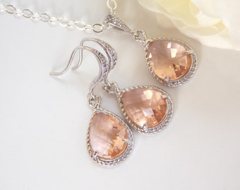 May include: A set of peach-colored teardrop-shaped crystal earrings and a matching necklace. The jewelry is silver-toned and features a delicate, beaded design.