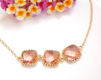 May include: A delicate gold chain necklace with three square-shaped pink crystals. The crystals are set in gold frames with a textured edge.