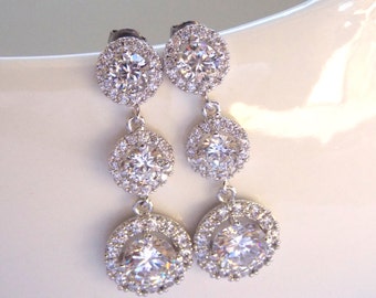 May include: Silver dangle earrings with three round clear crystal stones. The stones are surrounded by smaller clear crystals.