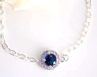Peut inclure: Un bracelet en chaîne argent avec une pierre précieuse bleue entourée de petites pierres précieuses claires.