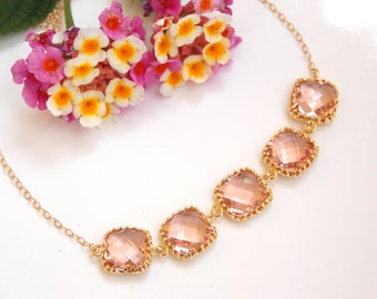 May include: A delicate gold chain necklace with five blush pink square-shaped crystals. The crystals have a faceted design and are set in gold.