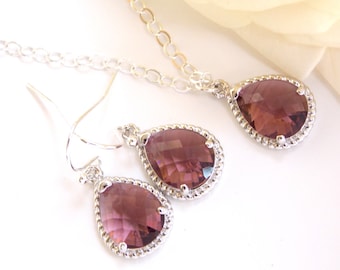 Puede incluir: Un collar y pendientes de plata con cristales morados en forma de lágrima. Los cristales están rodeados por un borde de cuentas plateadas.