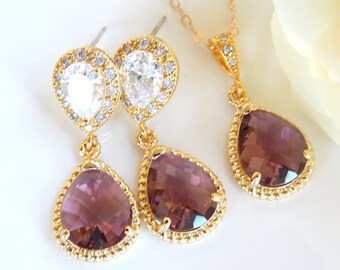 Puede incluir: Un conjunto de collar y pendientes de oro con un colgante de cristal morado en forma de lágrima y un colgante de halo de cristal transparente más pequeño.