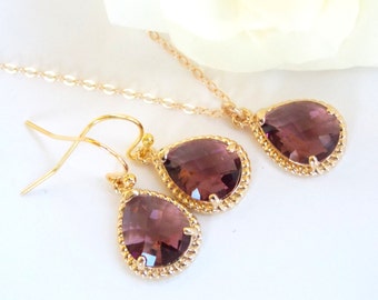 Puede incluir: Un collar y pendientes de oro con piedras de color púrpura en forma de lágrima. Las piedras están engastadas en un bisel de oro con un borde de cuerda.