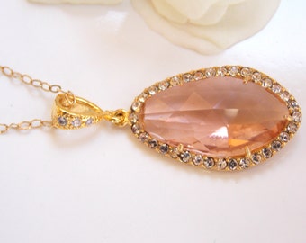 May include: A gold chain necklace with a pendant featuring a large, oval-shaped, light pink crystal surrounded by a border of small, clear rhinestones.