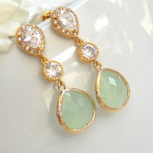 May include: Gold dangle earrings with a teardrop shaped green stone and clear crystal accents.