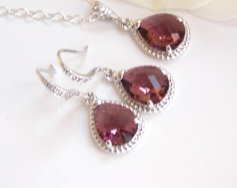 May include: A set of silver teardrop earrings and a matching necklace with a purple crystal in each pendant. The crystals are surrounded by a silver beaded border.