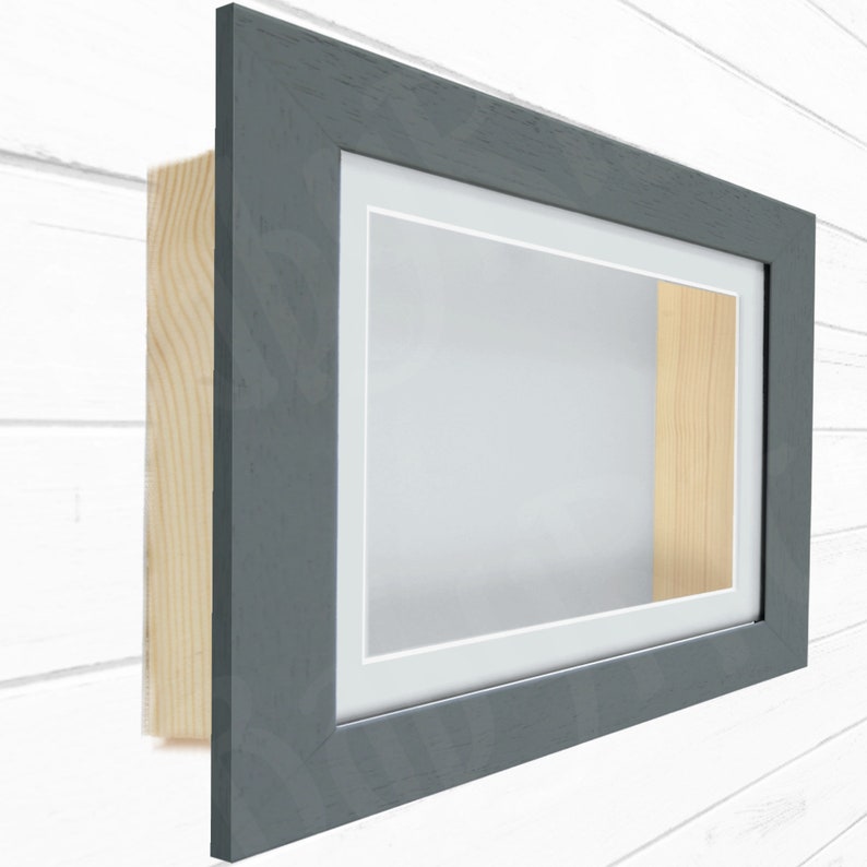 May include: A gray shadow box frame with a white mat and a wood backing. The frame is made of wood and has a simple, modern design.