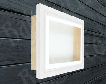 May include: White shadow box frame with a white mat and a wood backing. The frame is hanging on a dark wood wall.