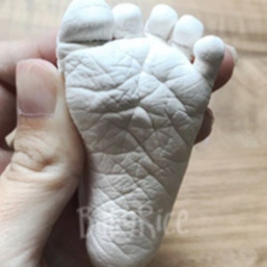 May include: A white plaster cast of a baby's foot, showing the details of the toes and the sole of the foot.