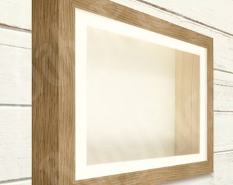 Puede incluir: Una caja de sombra de madera con un marco de madera clara y un paspartú blanco. La caja está vacía y lista para mostrar tus artículos favoritos.