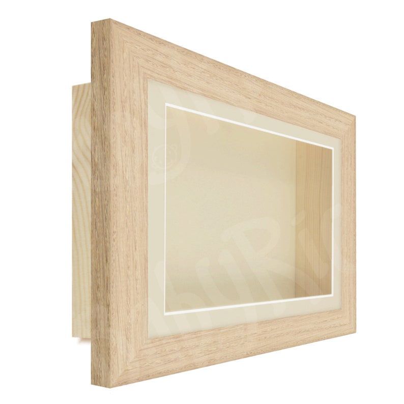 Puede incluir: Un marco de caja de sombra de madera clara con un passe-partout blanco y un frente de vidrio transparente.