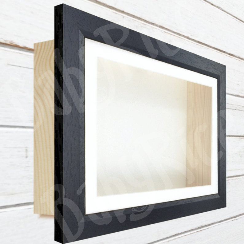 May include: A black wood shadow box frame with a white mat and a clear glass front. The frame is mounted on a white wood wall.
