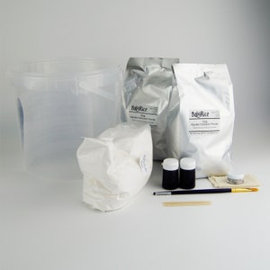 May include: A set of supplies for making alginate impressions. The set includes two bags of BabyRice alginate impression powder, a white plastic bucket, a white paper bag, two small black bottles, a small clear jar, a brown cloth, a wooden stick, and a paintbrush.