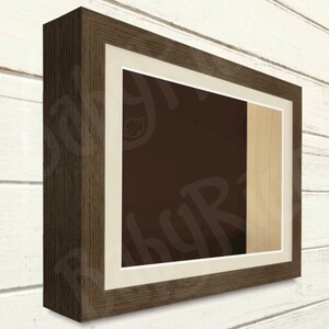May include: A dark brown wood picture frame with a white mount and a light wood insert. The frame is angled to show the side profile.