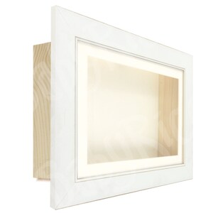 May include: White shadow box frame with a white mount and a clear glass front. The frame is made of wood and has a simple design.