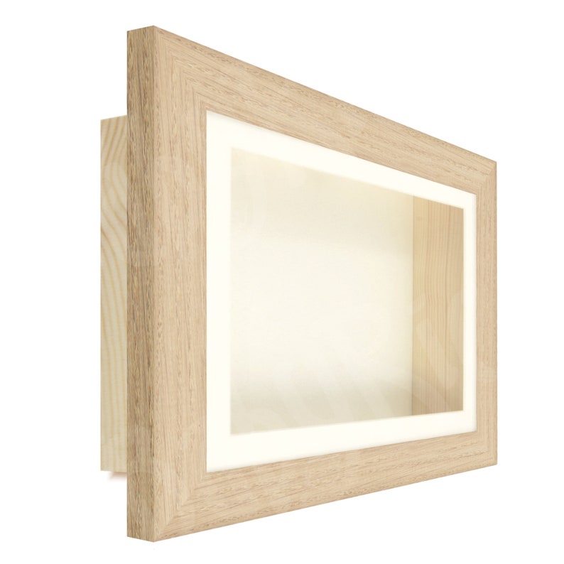 May include: A light wood shadow box frame with a white mat and a clear opening. The frame is perfect for displaying small items, such as jewelry, coins, or other collectibles.