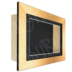 May include: A gold-colored wooden picture frame with a black mat and a white inner bevel. The frame has a shadow box design with a small opening on the right side.