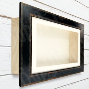 May include: A black wood shadow box frame with a white mount and a wood backing. The frame has a distressed finish.