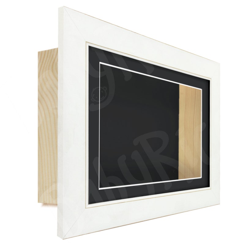 May include: White wooden picture frame with a black mount and a small wooden insert. The frame is designed to display a 3D object, such as a medal or a small sculpture.