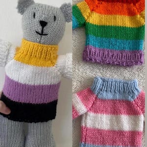 May include: A grey knitted teddy bear wearing a jumper with yellow, white, purple, and black horizontal stripes. Two additional knitted jumpers are shown: one with rainbow stripes and another with light blue, white, and pink horizontal stripes.