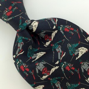 May include: A dark blue silk tie with a repeating pattern of skiers in various poses on a snowy mountain. The skiers are wearing colorful clothing and holding ski poles.
