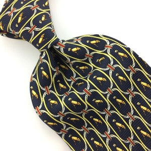 May include: A dark blue silk tie with a repeating pattern of yellow stylized birds in oval frames with red and white accents.