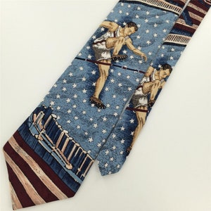 May include: A blue silk tie with a white star pattern and a repeated image of a man in a white uniform jumping over a hurdle. The tie has a red and white striped pattern at the bottom.
