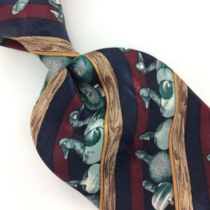 May include: A silk necktie with a repeating pattern of blue, green, and brown ducks on a striped background. The stripes are red, blue, and brown.