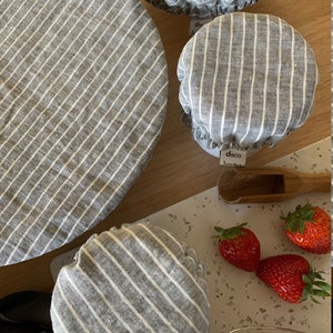 Peut inclure: Quatre couvercles de bol en tissu rayés gris et blancs de différentes tailles. Les couvercles sont en lin et ont un design simple et moderne. Les couvercles sont sur une surface blanche avec une cuillère en bois et des fraises.