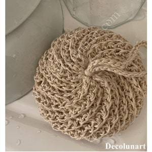 Peut inclure: Gros plan sur une éponge de bain en crochet beige. L'éponge est faite de fibres naturelles et a une surface texturée. C'est une alternative durable et écologique aux éponges en plastique.