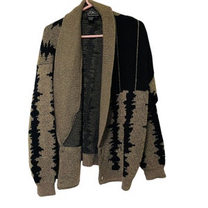 May include: A beige and black patterned cardigan sweater with a shawl collar. The sweater has a geometric design in black and beige, with a black panel on the right side. The brand name "JONIE" is visible on the label.