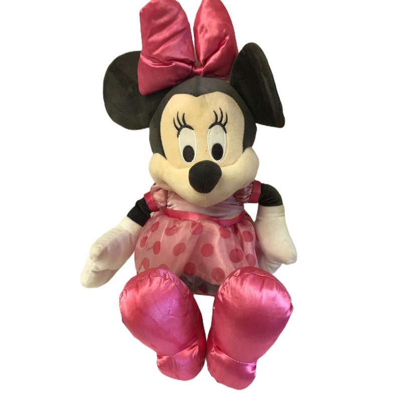 Pu&ograve; includere: Una bambola di peluche di Minnie Mouse con un vestito rosa a pois, fiocco e scarpe abbinate. La bambola ha orecchie nere, naso nero e guanti bianchi. La bambola &egrave; seduta e ha un'espressione amichevole.