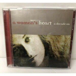 Puede incluir: Una caja de CD con el título "a woman's heart | a decade on" en texto blanco sobre un fondo gris. La portada presenta una imagen sepia del rostro de una mujer. La caja tiene un lomo rojo.