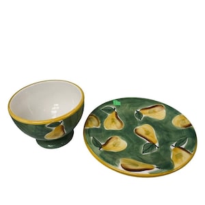 May include: A ceramic bowl and plate set. The bowl has a white interior and a green exterior with yellow pear designs. The plate is oval-shaped, green with yellow pear designs, and a yellow rim. The set is suitable for serving food.