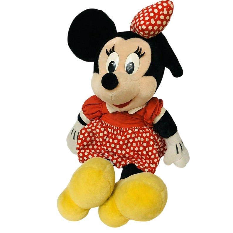 May include: A plush Minnie Mouse doll. The doll has black ears, a red and white polka dot bow, and a red dress with white polka dots. Her large yellow feet are visible.