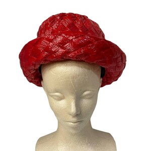 May include: A bright red woven hat with a wide brim and a rounded crown. The hat has a textured, basket-weave appearance and a black interior band. The hat is displayed on a mannequin head against a white background.