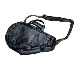 May include: Black leather tennis racket bag with a shoulder strap and a handle. The bag has a quilted design on the main compartment and a smaller pocket on the front. The bag is designed to carry a tennis racket and other accessories.