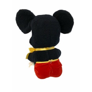 May include: A plush Mickey Mouse toy, viewed from the back, features a black body and large ears. The toy wears red shorts and a yellow bow tie. The toy is a classic Disney character.