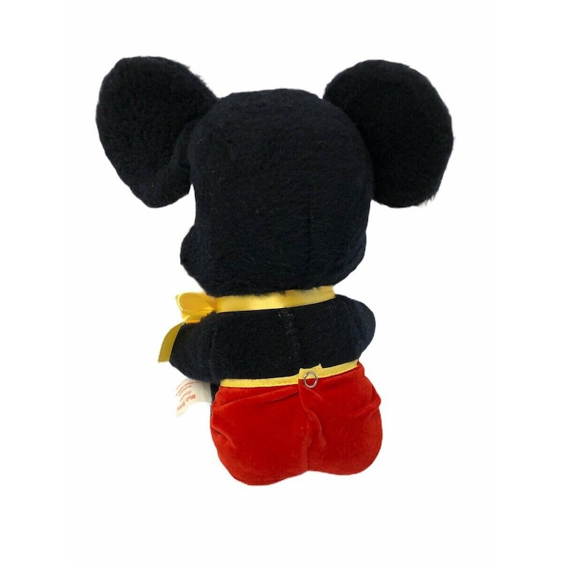 May include: A plush Mickey Mouse toy, viewed from the back, features a black body and large ears. The toy wears red shorts and a yellow bow tie. The toy is a classic Disney character.