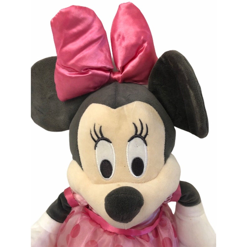 Pu&ograve; includere: Bambola di peluche di Minnie Mouse con un grande fiocco rosa, orecchie nere e un vestito rosa a pois. La bambola ha ciglia ricamate e un viso color crema. Un personaggio popolare della Disney.
