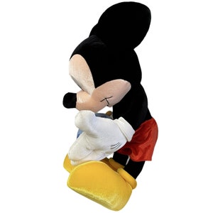 Puede incluir: Un peluche de Mickey Mouse, con cuerpo negro, cara y orejas color beige, guantes blancos, pantalones cortos rojos y zapatos amarillos. El ic&oacute;nico personaje est&aacute; en una pose de perfil, con una ligera inclinaci&oacute;n.