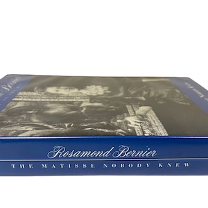 Może przedstawiać: Książka zatytułowana "Rosamond Bernier: The Matisse Nobody Knew" z niebieską okładką. Okładka zawiera czarno-biały obraz malarstwa. Tytuł jest w białym skrypcie i blokowych literach.