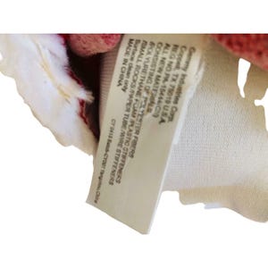 May include: A close-up of a tag with text. The tag is white with black text and is attached to a red and white fabric. The tag lists the materials and manufacturer information.
