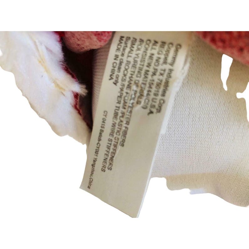 May include: A close-up of a tag with text. The tag is white with black text and is attached to a red and white fabric. The tag lists the materials and manufacturer information.